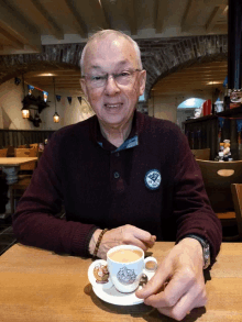 an older man sitting at a table with a cup of coffee in front of him