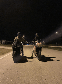 two motorcycle riders are standing next to each other on the road at night