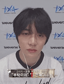 a young man wearing headphones is standing in front of a wall that says weverse