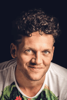 a man with curly hair is wearing a white shirt with a floral print