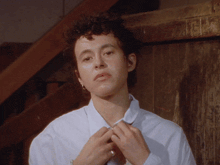 a woman with curly hair adjusts her white shirt