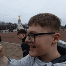 a young man wearing glasses stands in front of a statue of a woman