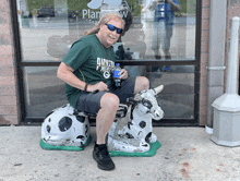 a man wearing a green shirt that says dairy north g is sitting on a cow statue