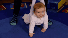 a baby is crawling on a blue rug with a person 's legs