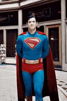 a man in a superman costume is standing in front of a store .