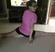 a girl in a pink shirt is doing a split in front of a tv