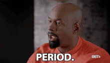 a man with a beard is wearing an orange shirt that says period