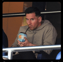 a man in a grey hoodie drinks from a cup with the argentina flag on it