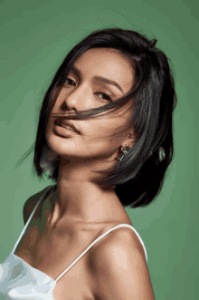 a woman with her hair blowing in the wind is wearing a white tank top