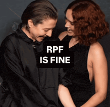 two women standing next to each other with a sign that says rpf is fine on it