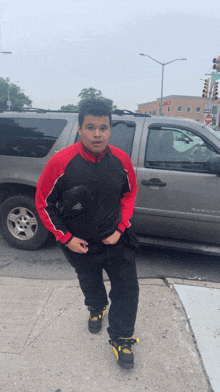 a man in a red and black jacket stands in front of a silver suv that says suburban