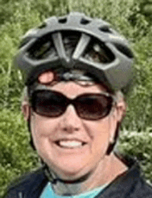 a woman is wearing a helmet and sunglasses and smiling .