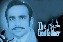 a man with glasses and a mustache is standing in front of a poster for the godfather