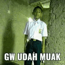 a boy in a school uniform is standing in front of a wall with a meme .