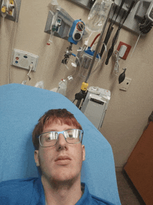 a man wearing glasses is laying in a hospital bed in front of a machine that says ' ambulance ' on it