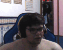 a shirtless man wearing glasses and headphones sits in a chair