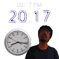 a man is standing next to a clock that says 20:17