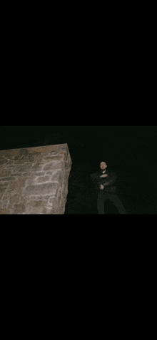 a man is standing next to a brick wall at night .