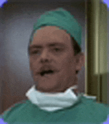 a man wearing a green surgical gown and a surgical cap is standing in a room .