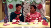 two men wearing ugly sweaters are eating cookies