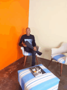 a man sits in a chair with his legs crossed and a book on a blue striped ottoman