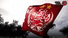 a red and white flag with arabic writing on it is flying in the wind