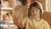 a young boy in a yellow shirt is holding a green object in his hand