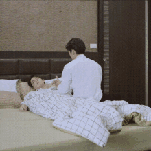 a man is standing next to a man laying on a bed .