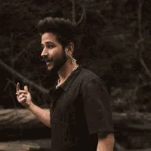 a man with a beard and mustache wearing a black shirt is standing in front of a wooden bridge .