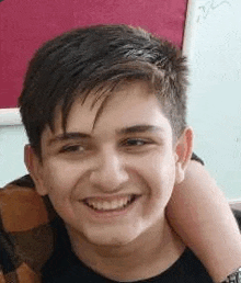 a young boy is smiling for the camera while sitting in front of a whiteboard .