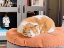 an orange and white cat sleeping on a pumpkin shaped pillow