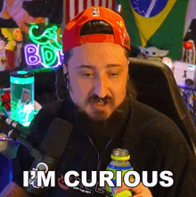 a man with a beard is sitting in front of a microphone and says i 'm curious
