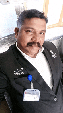 a man with a mustache wears a black suit and a name tag that says security