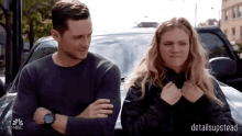 a man and a woman are standing next to each other in front of a car with nbc written on the bottom