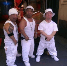 three men wearing white shirts and hats are standing next to each other on a sidewalk .