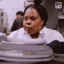 a woman in a white shirt is standing in front of a stack of plastic containers with the letters be on the bottom right