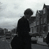 a black and white photo of a man walking down a street with a red truck that says barking on it