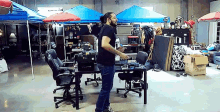 a man with a beard is standing in front of a desk in a room with a lot of chairs .