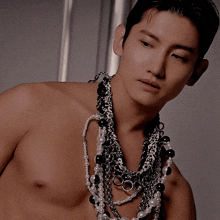 a shirtless man is wearing a necklace with pearls and chains around his neck