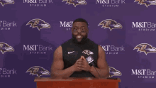 a man stands at a podium with a microphone in front of a purple backdrop that says m & t bank stadium