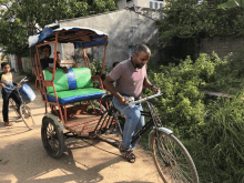 a man riding a bicycle pulling a rickshaw with a green and blue seat