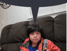 a young boy is sitting on a brown couch holding a video game controller .