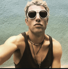 a man wearing sunglasses and a black tank top looks at the camera
