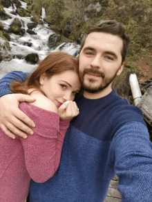 a man and a woman are posing for a picture in front of a waterfall