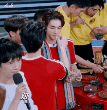 a group of young men are sitting around a table eating food . one of the men is wearing a red shirt .