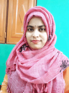 a woman wearing a pink scarf and a hijab looks at the camera