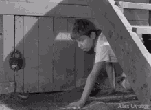 a black and white photo of a boy crawling through a wooden door with alex uyutor written on the bottom right