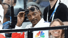 snoop dogg is wearing sunglasses while sitting in the stands at a tennis match