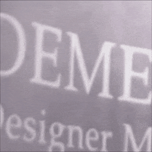 a close up of the word deme designer on a white background