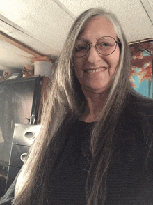 a woman with long gray hair wearing glasses and a black shirt